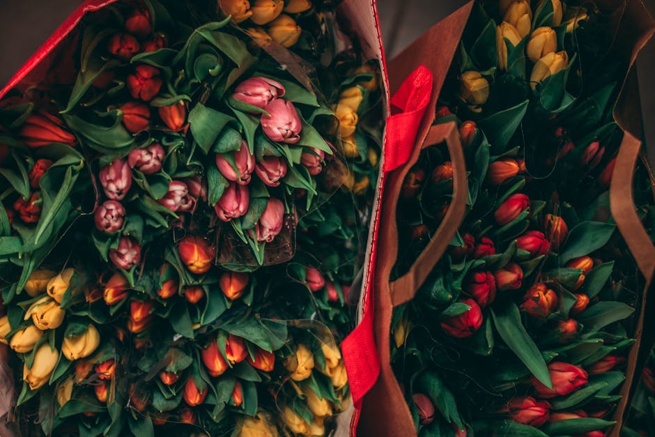 A collection of bouquets featuring tulips in vibrant shades of pink, red, and yellow, arranged in clear plastic wrapping and placed inside open paper bags. The flowers display fresh, slightly glossy p